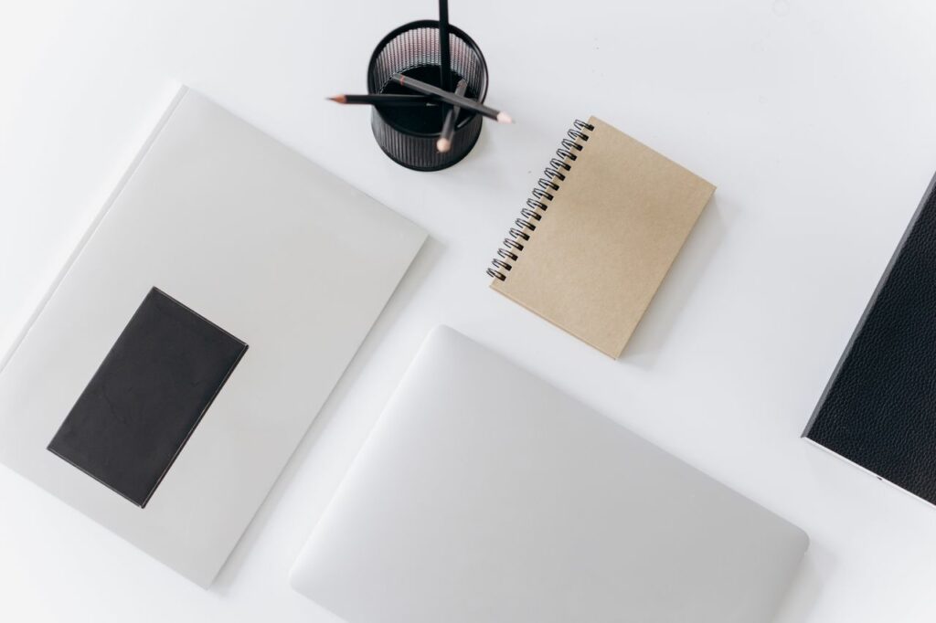 Top view of modern laptop with notebooks and cup of pencils composed on white table in office