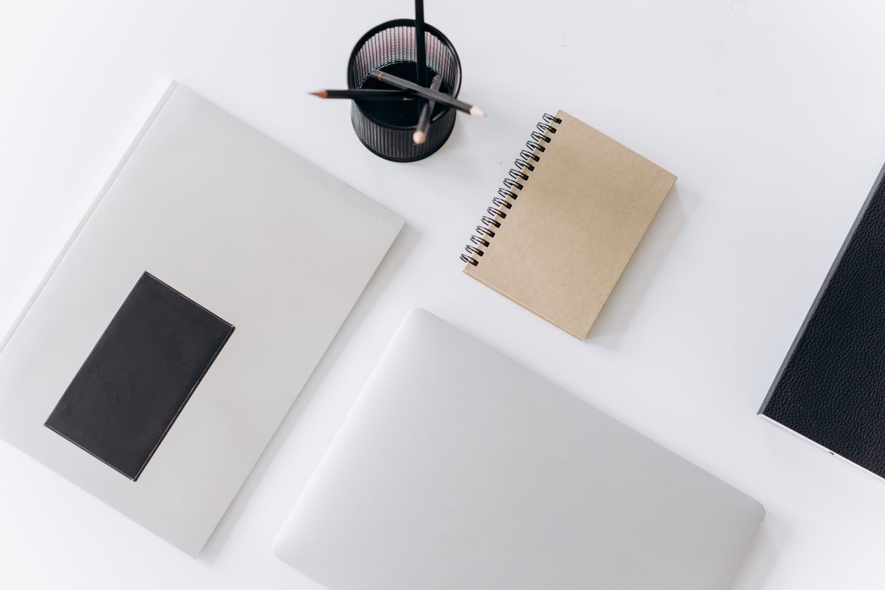 Top view of modern laptop with notebooks and cup of pencils composed on white table in office